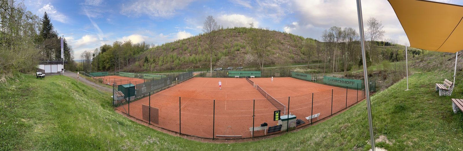 Panoramablick auf die Tennisanlage des TC Blau-Weiss Attendorn mit den drei Sandplätzen und Hang im Hintergrund